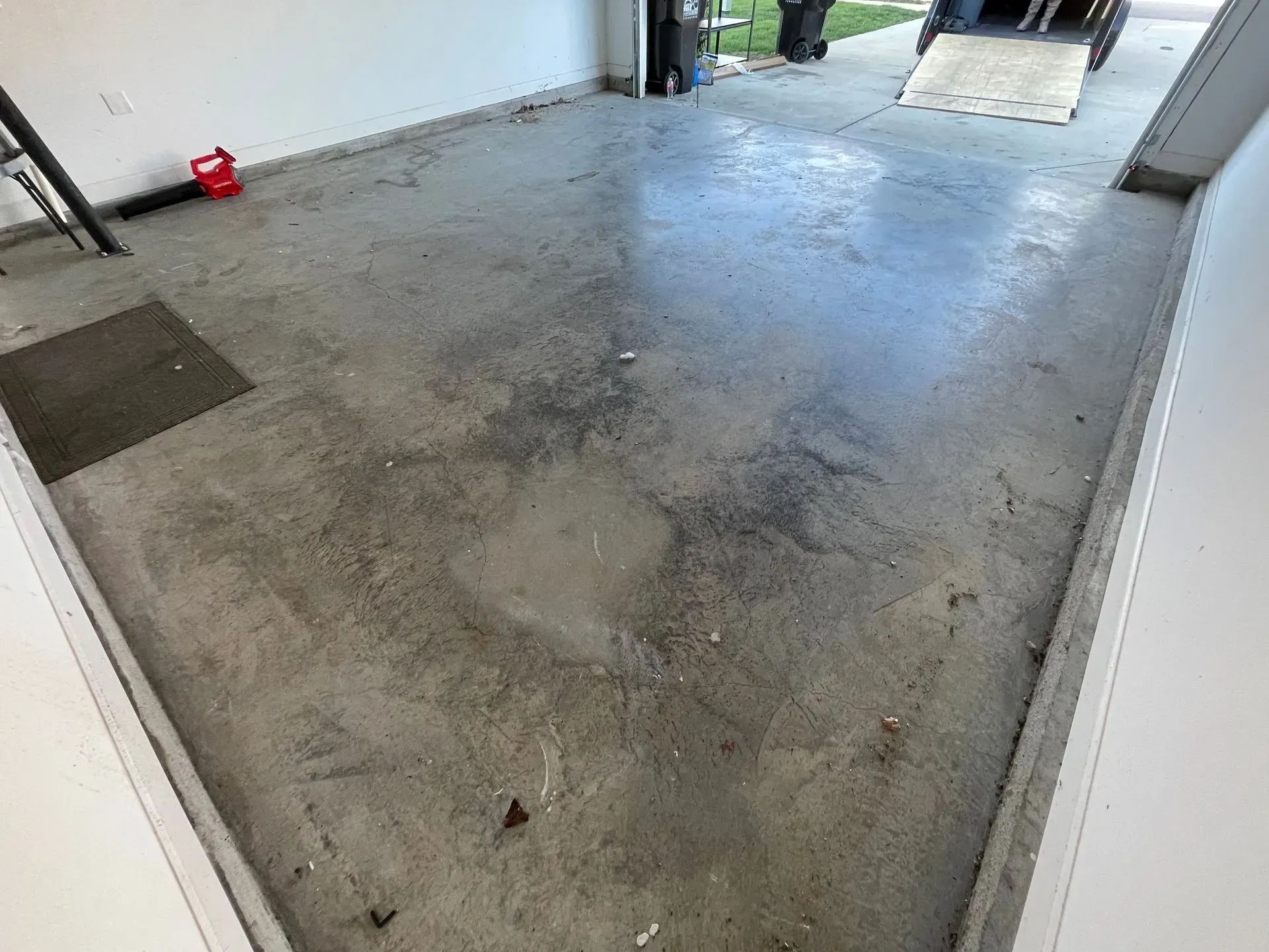 Concrete garage floor, speckled with dark stains, with a ramp in the background.