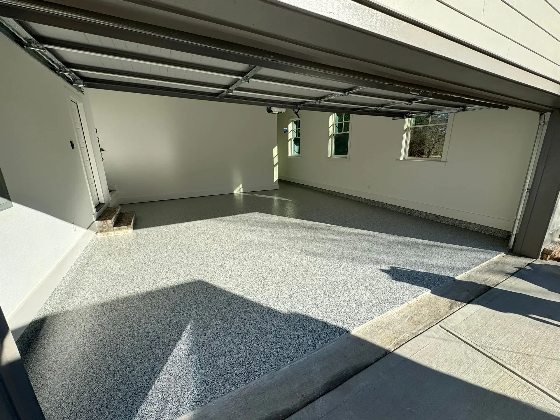 A newly painted garage with a speckled gray floor and white walls. Sunlight streams through the open door.