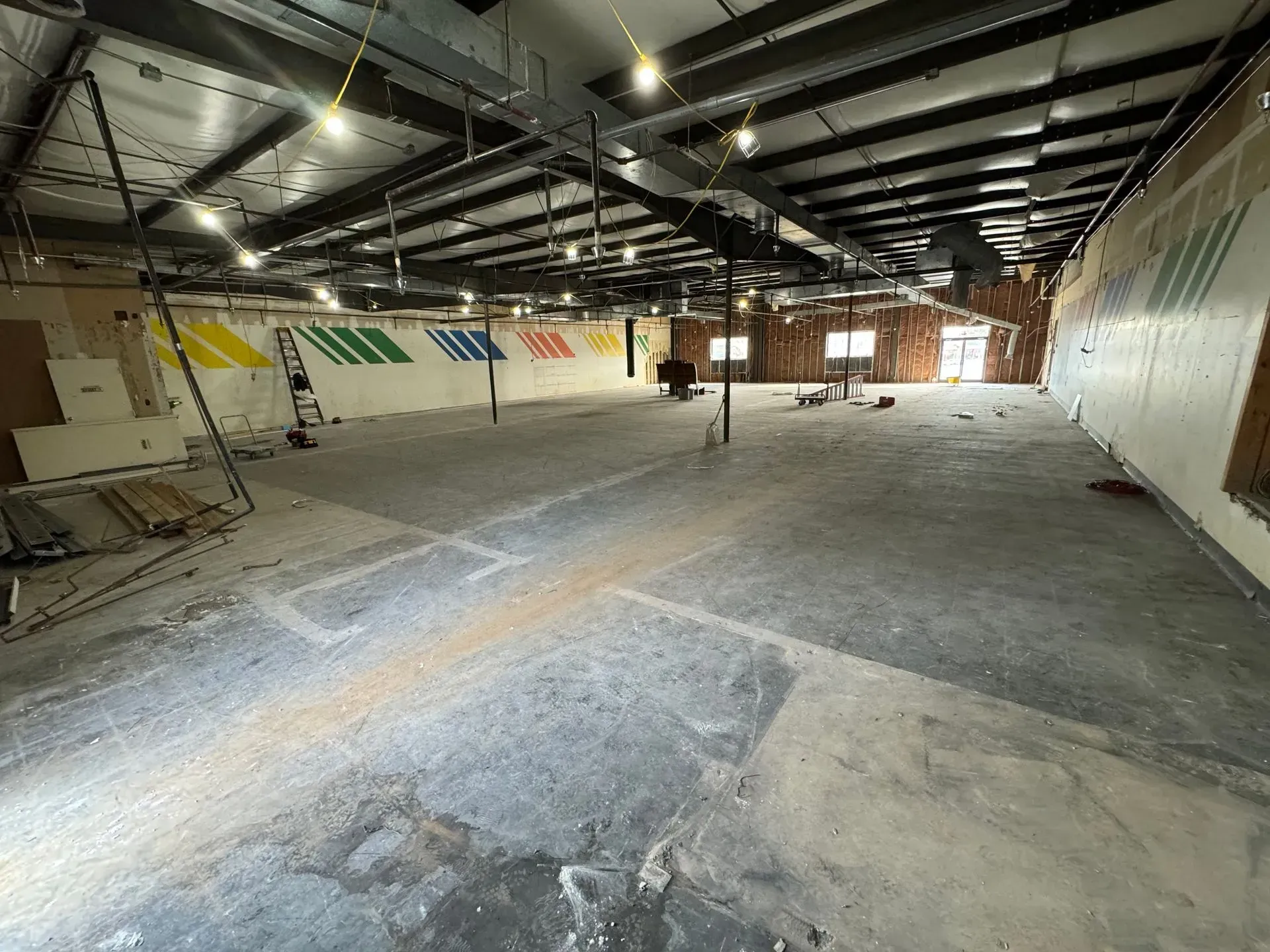 An empty commercial space undergoing renovation with exposed ceiling, and a colorful mural on the wall.