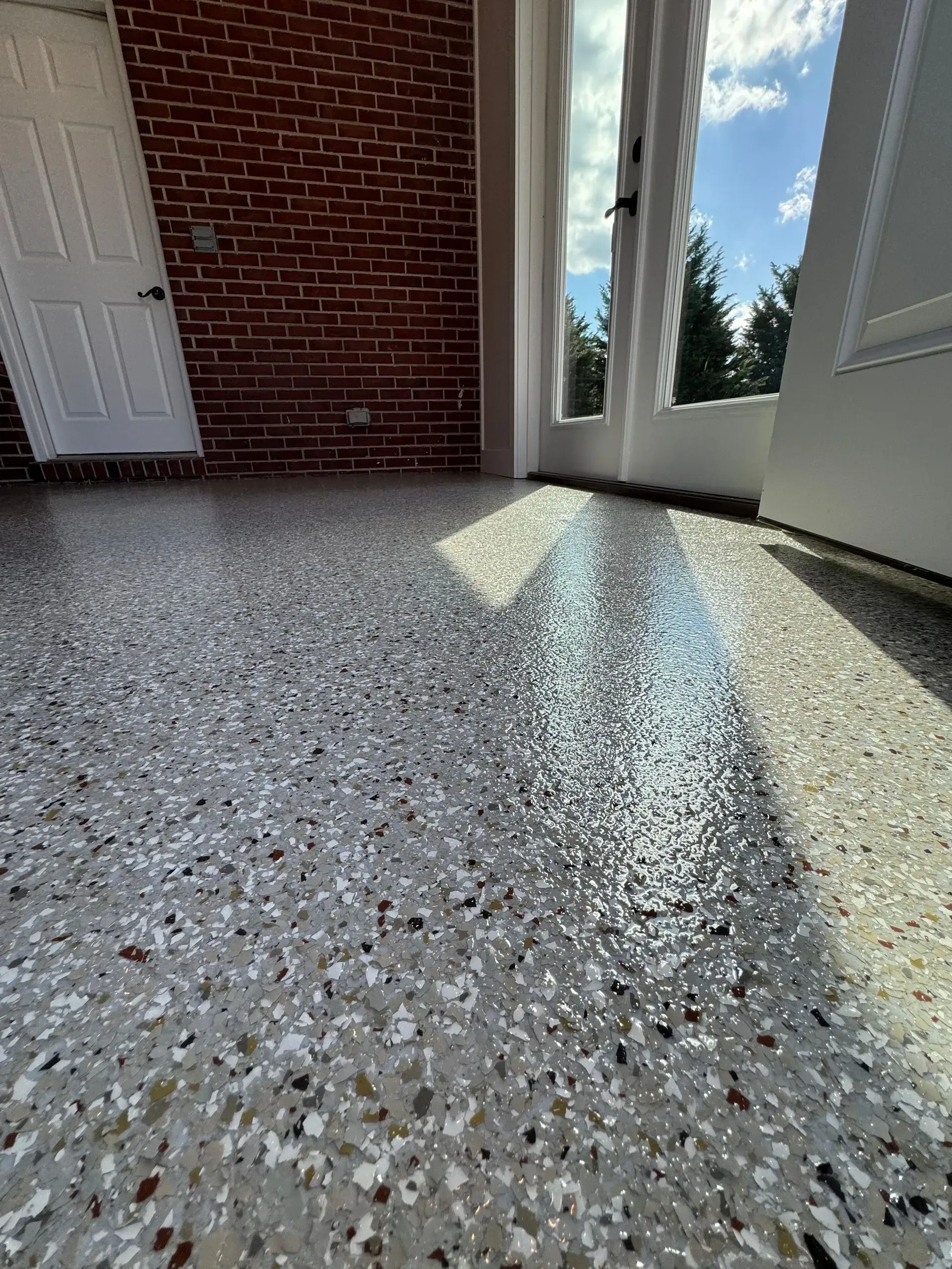 Terrazzo floor with sunlight and brick wall, next to a door and window.