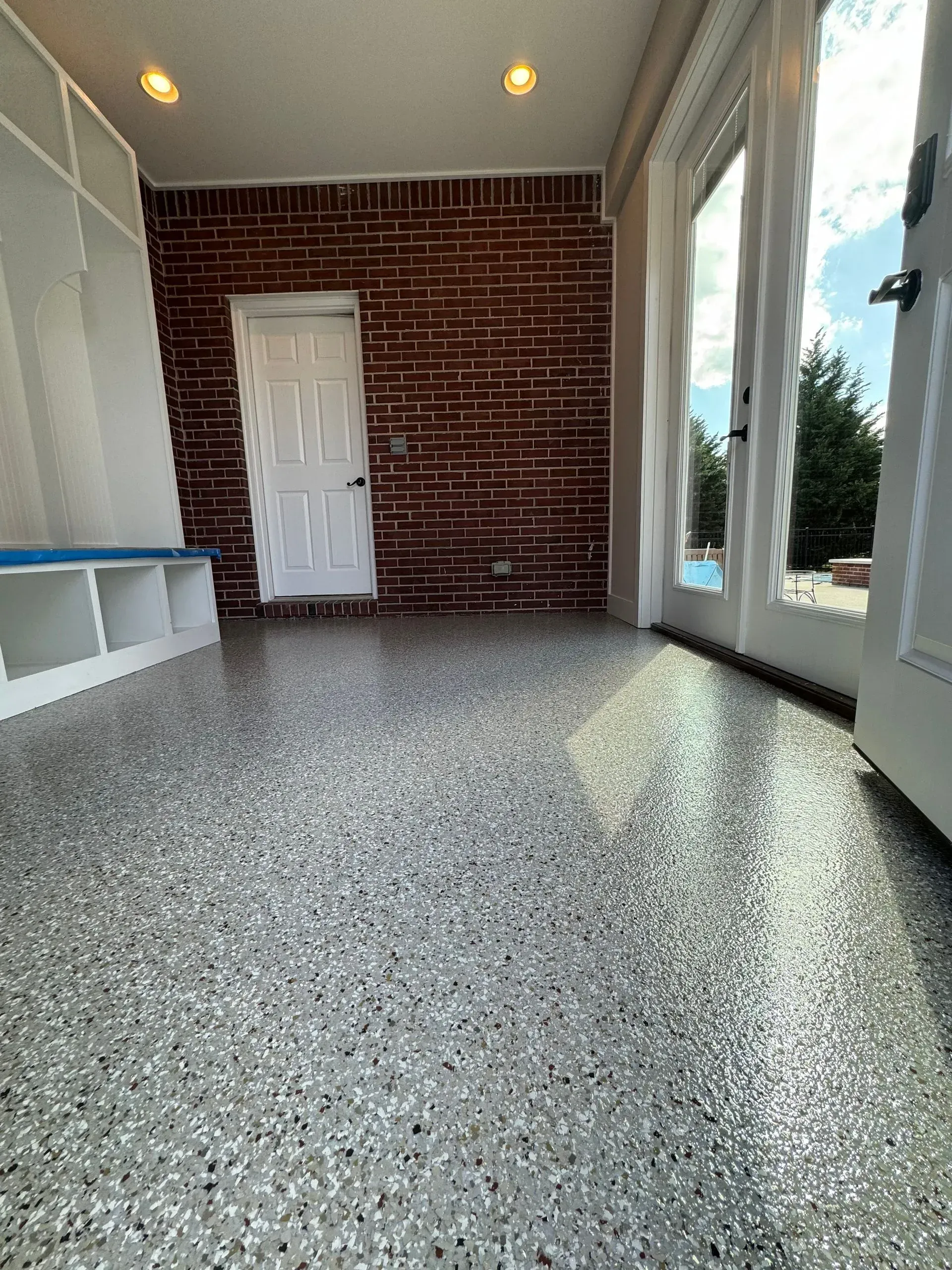 Garage with speckled floor, brick wall, white door, and French doors leading outside.