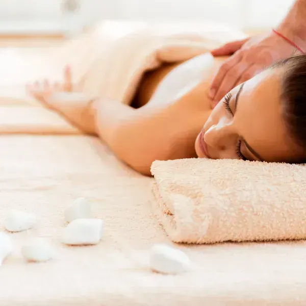 Person receiving a back massage on a towel-covered spa table with white stones nearby