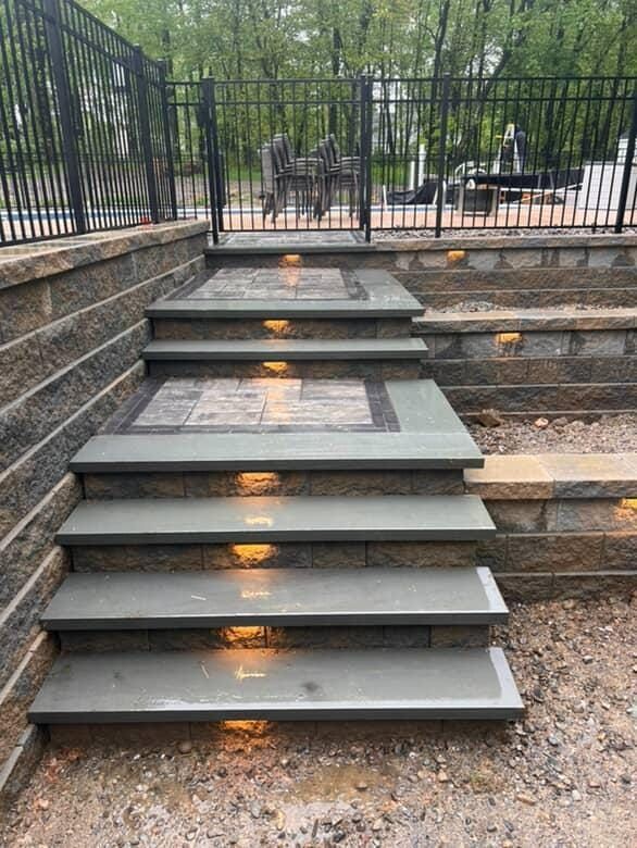 Stone steps with built-in lights, leading up to a patio area with a black fence.