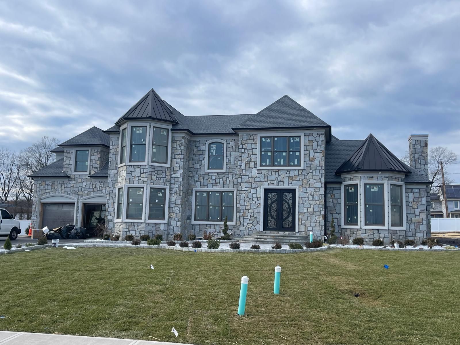 Large gray stone house with multiple windows and turrets on a cloudy day.