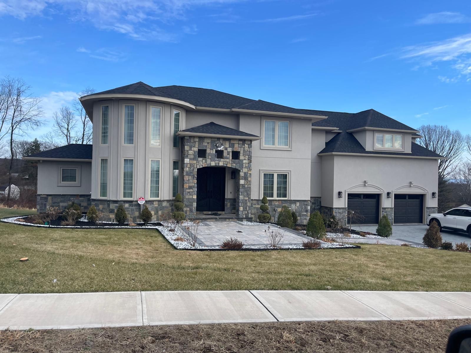 Large light gray house with black roof, stone entrance, and two-car garage on a grassy lawn.