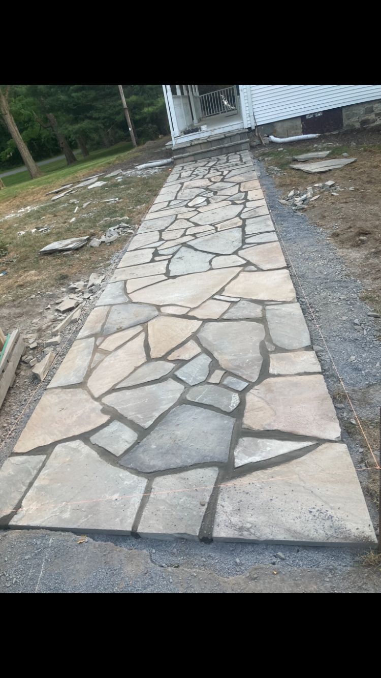 Stone walkway leading to a house under construction; gray stones and mortar.