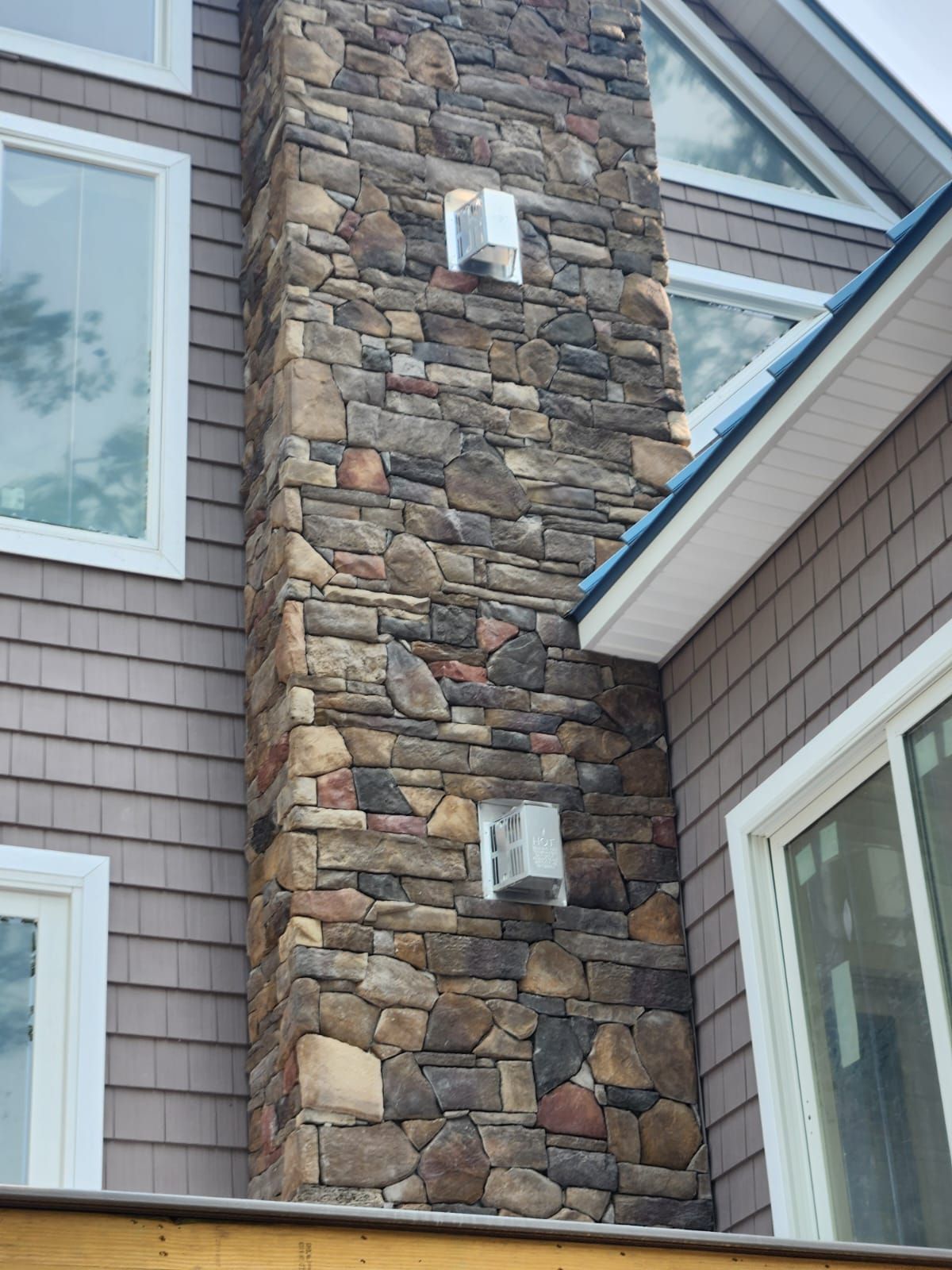 Stone chimney on a house with brown siding and white-framed windows.
