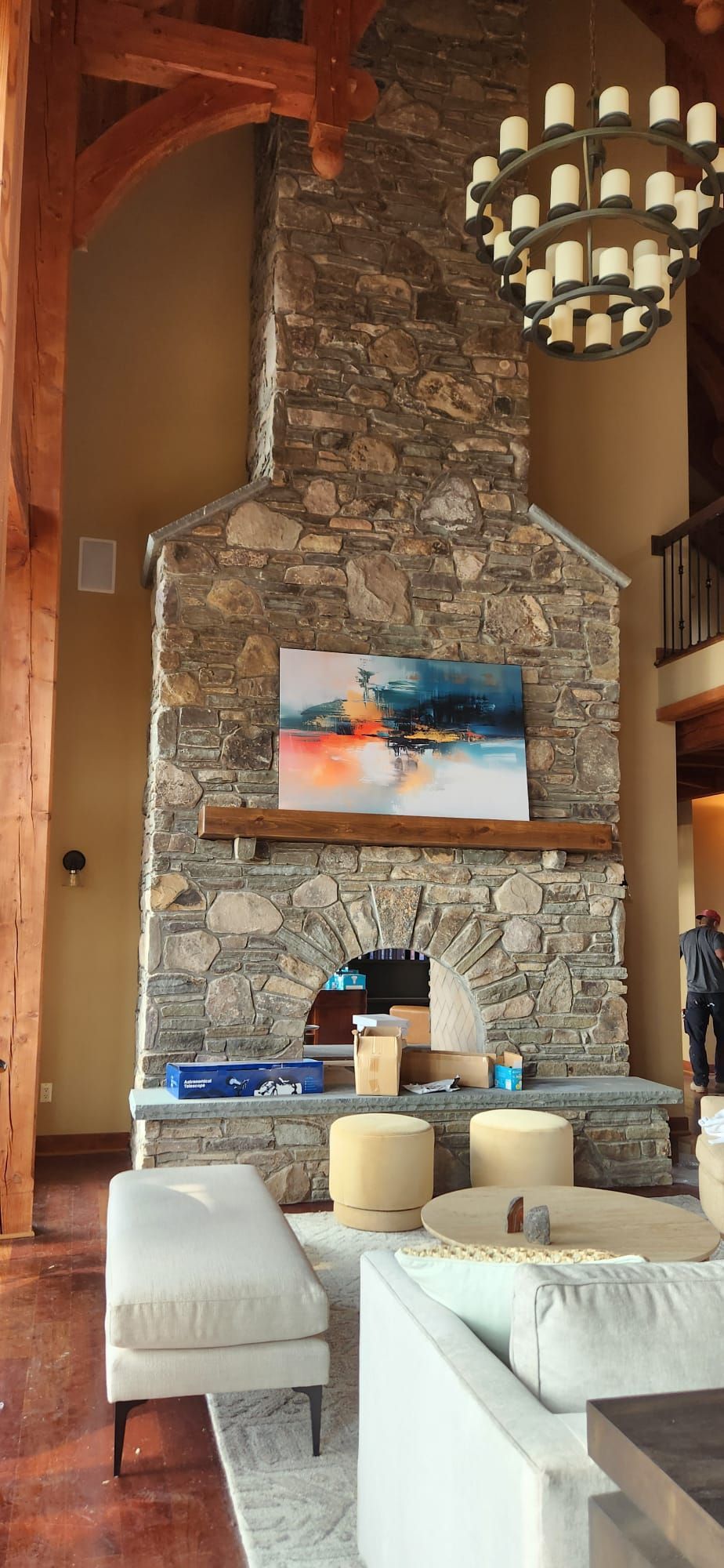 Stone fireplace in a living room with abstract artwork and a chandelier. Beige and white furniture is in front.