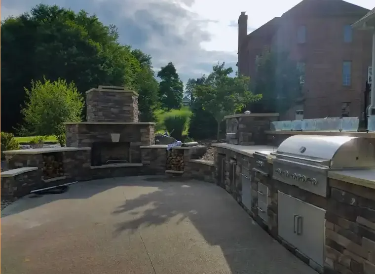 Outdoor kitchen with stone features, fireplace, and built-in grill on a patio.