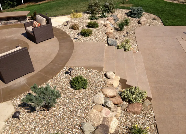 Patio with seating, pathway, rock garden, and lush landscaping. Brown and beige tones.
