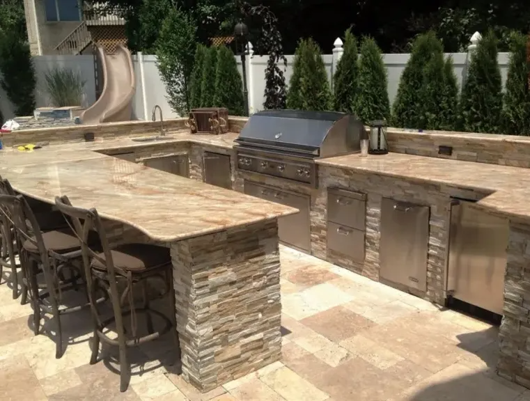 Outdoor kitchen with stone counters, stainless steel grill, bar seating, and a slide.