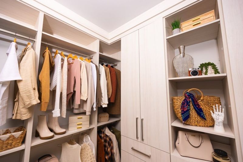 Walk-in closet with neutral-toned clothing, shelves with accessories, and a straw bag.
