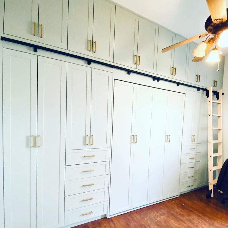 Light green built-in storage cabinets with gold handles. Includes a Murphy bed and a rolling ladder.