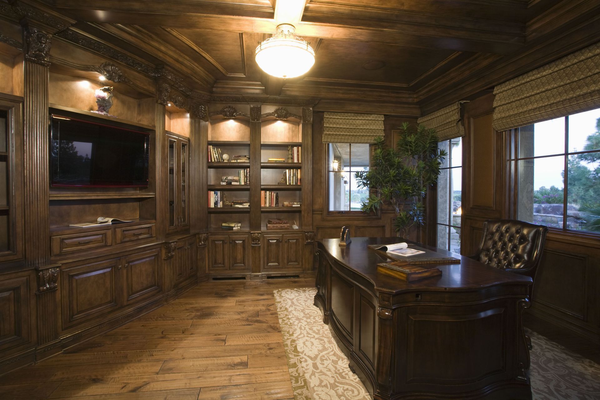 Elegant, wood-paneled home office with large desk, built-in shelves, TV, and window with a view.
