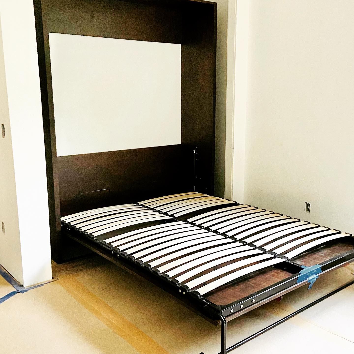 Dark brown wall bed frame in a room with light walls and floor. Bed is open.