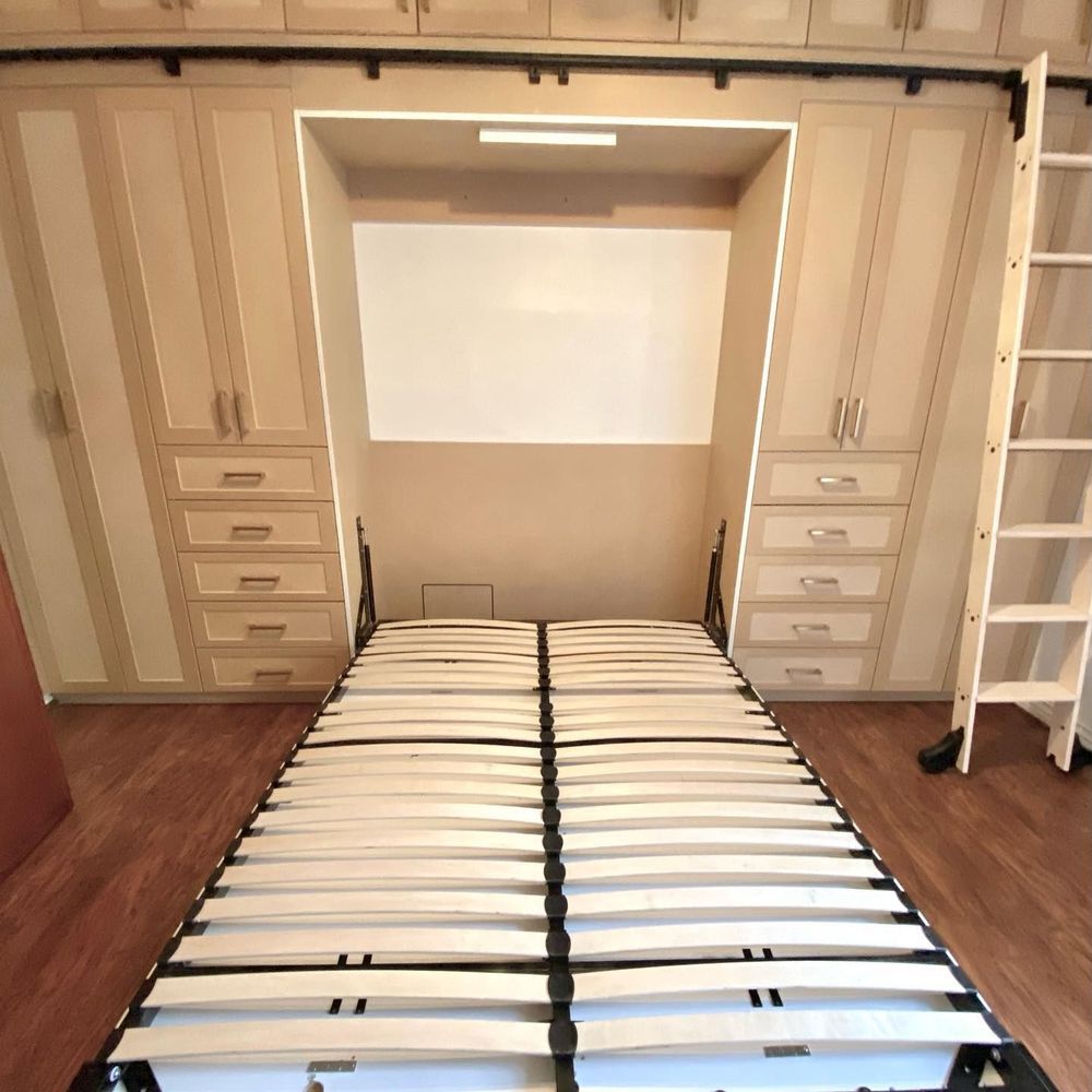 A wall-mounted Murphy bed is open. Built-in cabinetry surrounds it. Ladder stands at right.