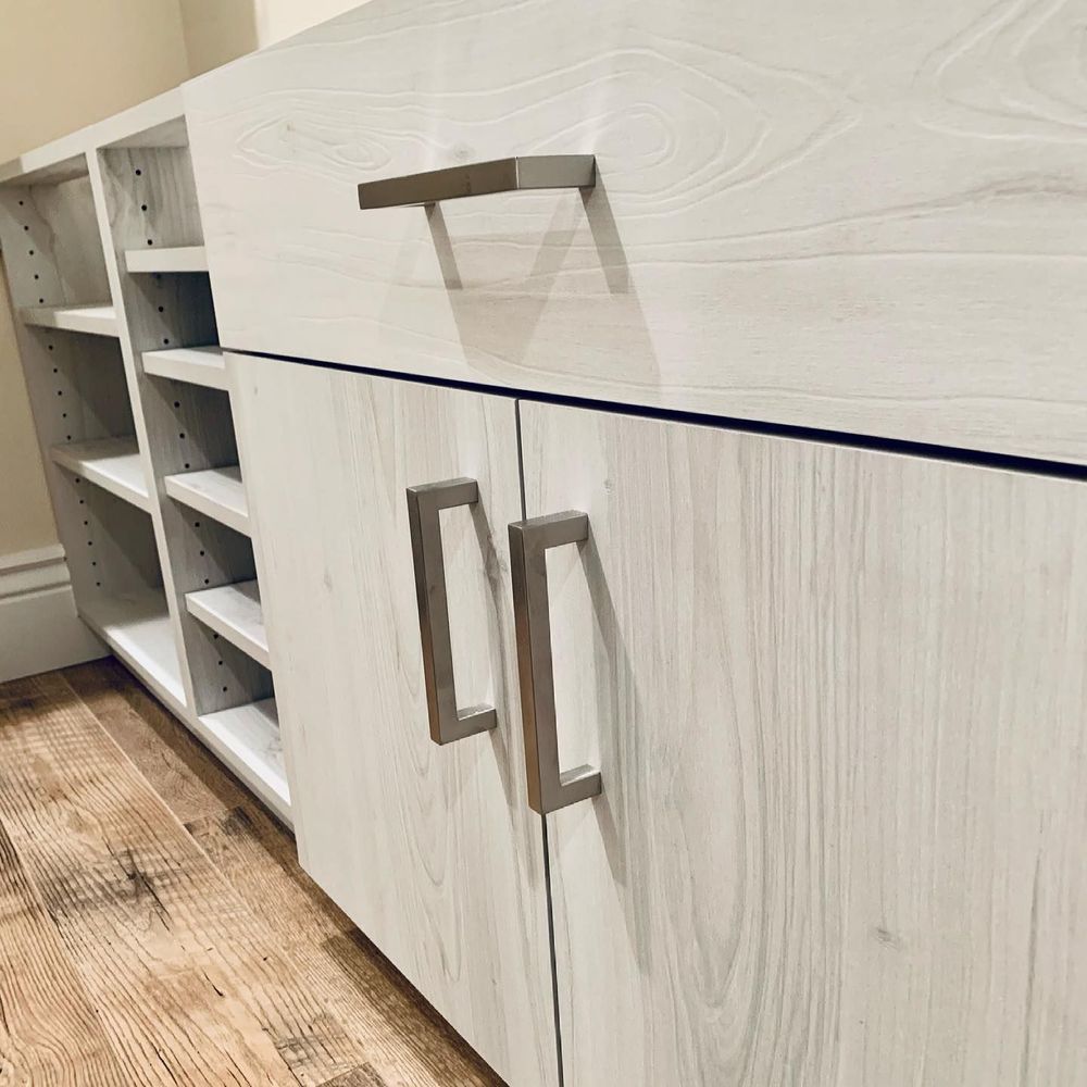 Light-colored wood cabinet with silver hardware. Open shelving to the left. Wooden flooring.