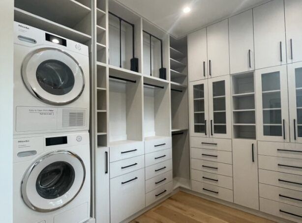 Walk-in closet with stacked washer and dryer, white cabinets, and black hardware.