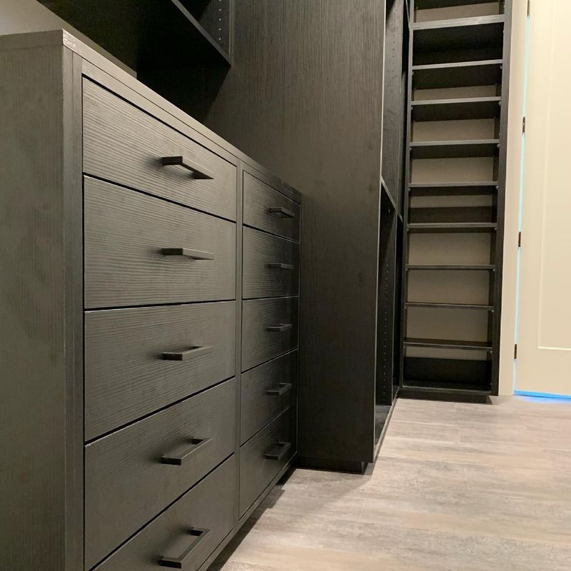 Black closet with drawers and shelves; neutral wood-look floor.