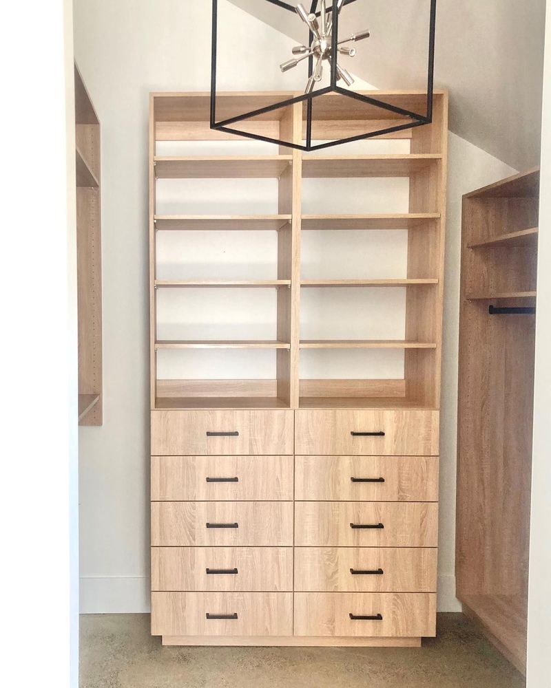 Wooden closet shelving unit with drawers, shelves, and a modern light fixture.