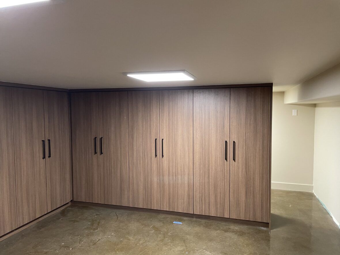 Brown wood grain storage cabinets installed in a room with a cement floor and overhead lighting.