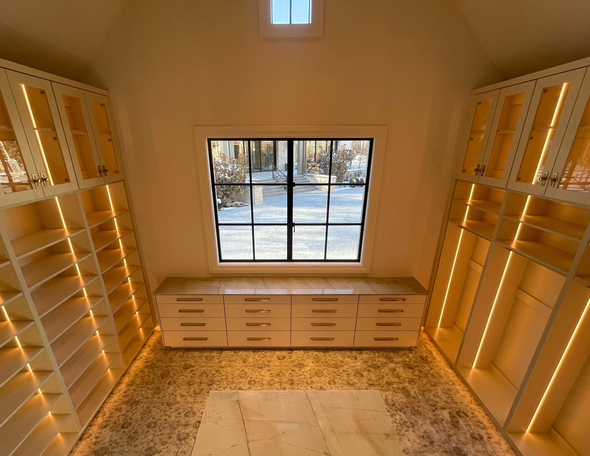 Walk-in closet with built-in shelving and drawers. A window and rug add light and warmth to the space.