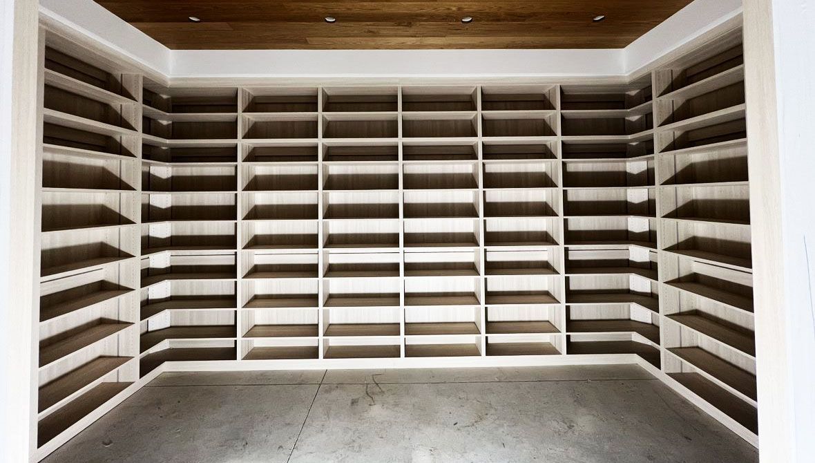 Empty built-in white shelves filling a room; wood ceiling, concrete floor.