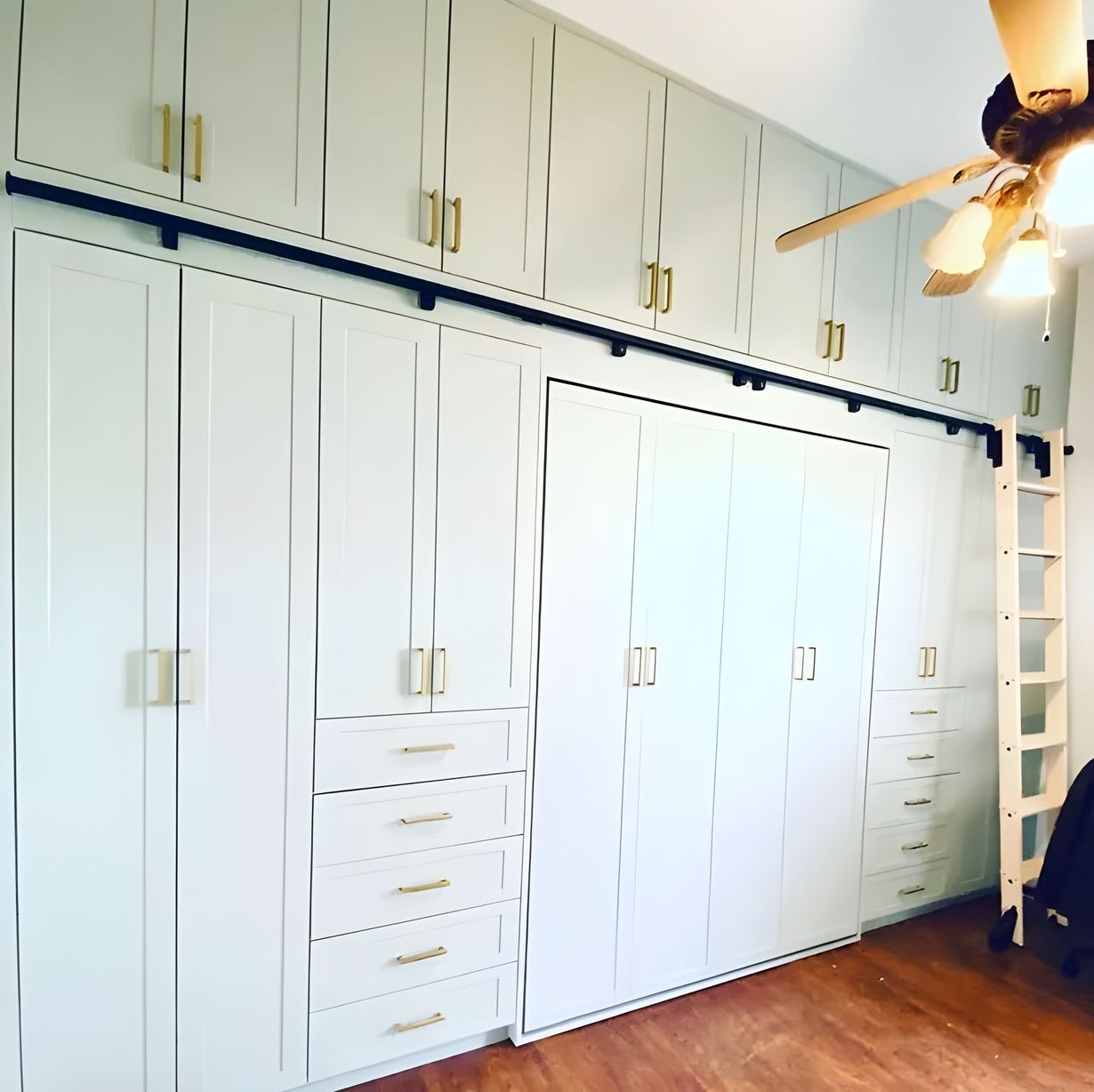 Built-in white storage cabinets with gold handles. A black bar and light wood ladder are attached.