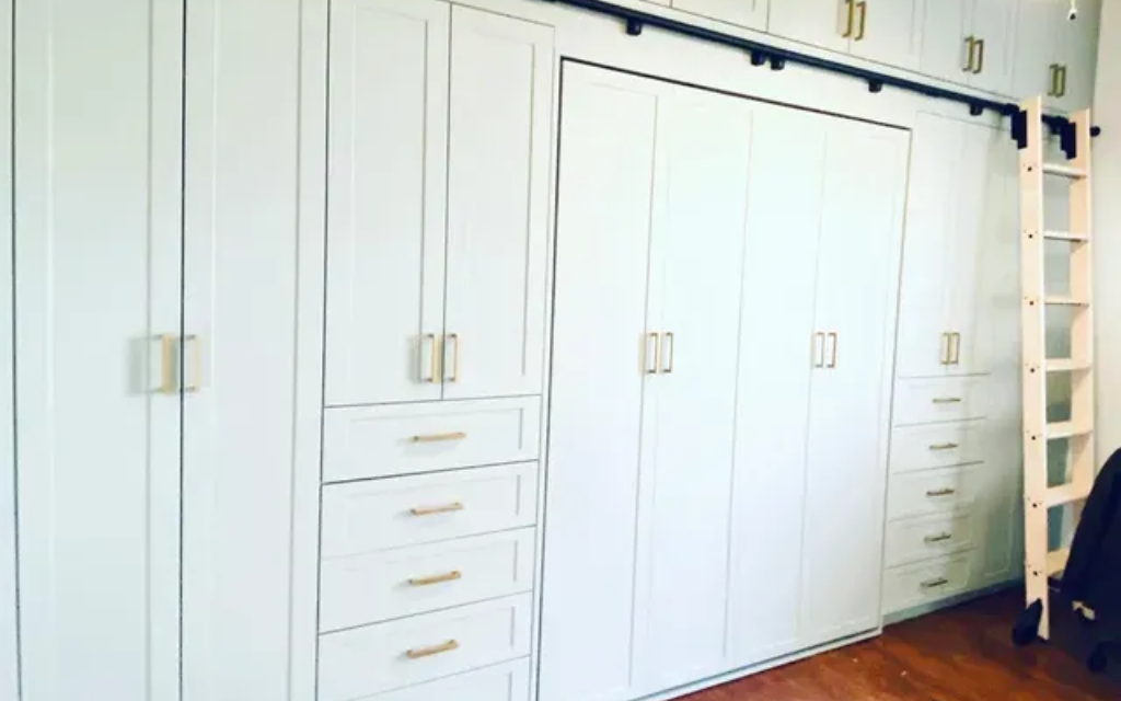 Built-in white storage cabinets with gold handles. A black bar and light wood ladder are attached.