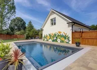 Rectangular pool in a backyard with a white house, mural, and blue sky.