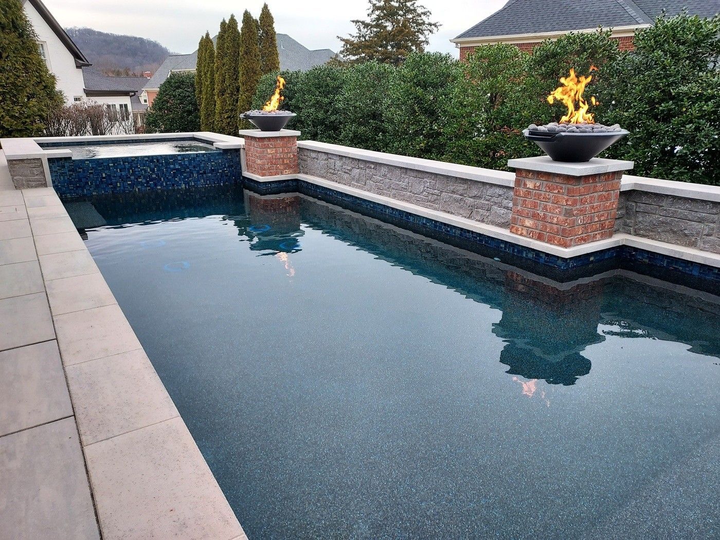 Pool with blue water and fire features, surrounded by stone and greenery.