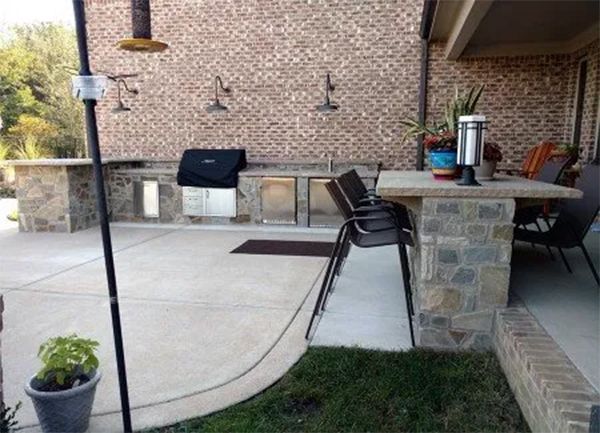 Outdoor kitchen with brick wall, concrete countertop, grill, and bar seating.