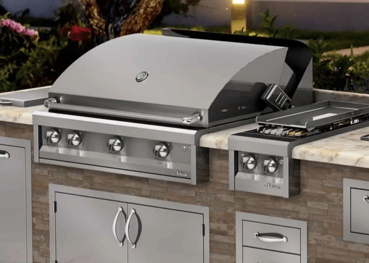 Stainless steel outdoor grill and side burner built into a stone and steel kitchen island.