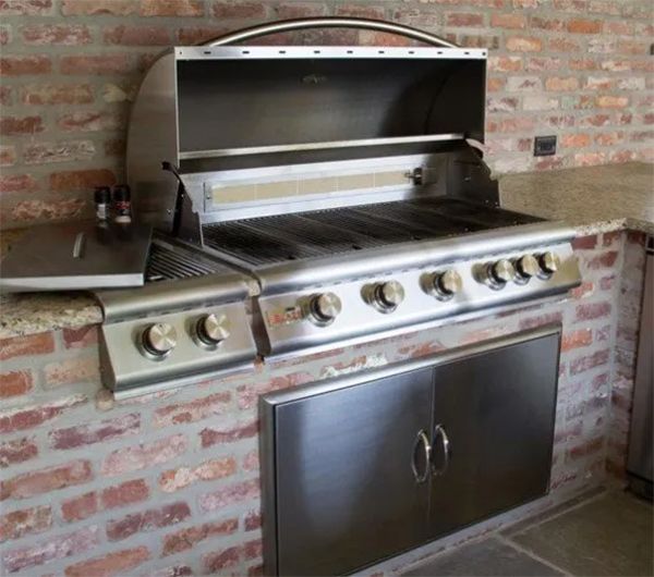 Stainless steel outdoor grill built into a brick wall with lower storage cabinets.