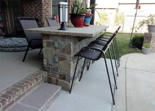 Outdoor bar with stone facade, concrete countertop, and metal bar stools.