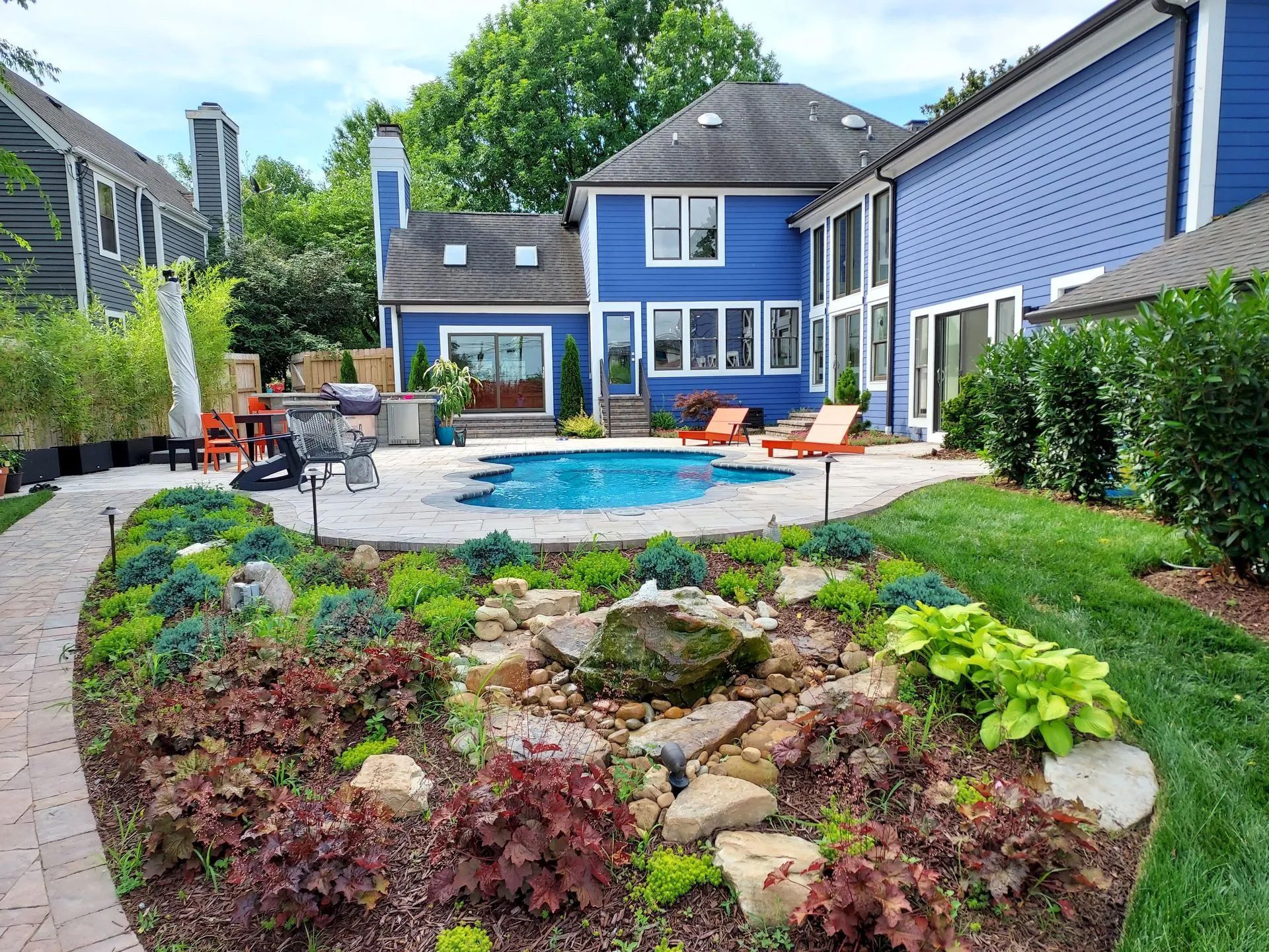 Backyard with blue house, pool, and landscaped garden with stone pathway.