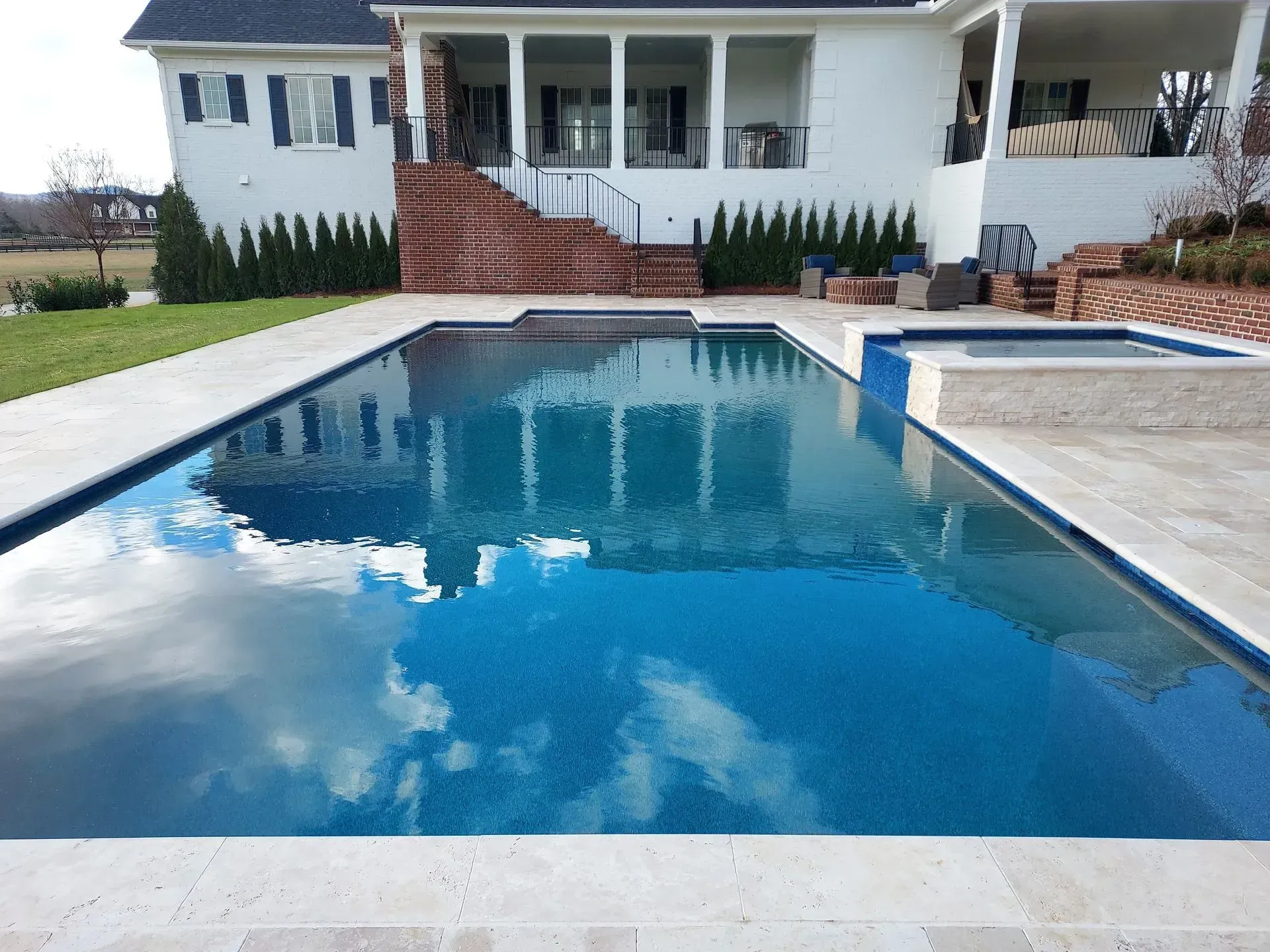 Pool with blue tile reflecting sky, next to a house with porch and steps.