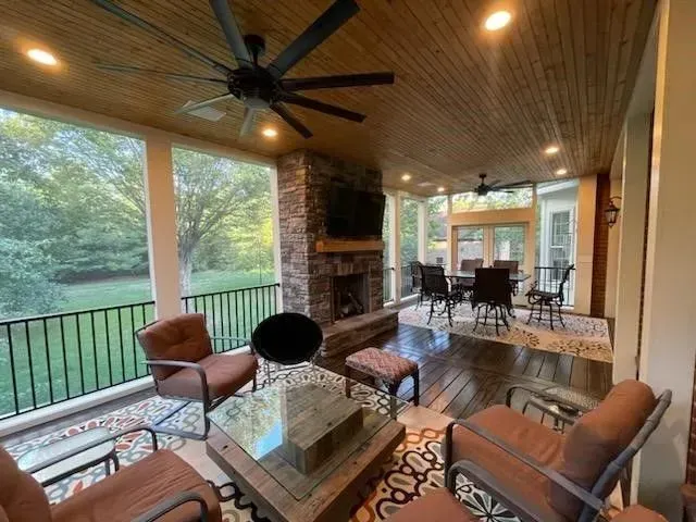 Screened-in porch with fireplace, seating, and dining area. Dark wood ceiling and floor, stone fireplace, and ceiling fans.