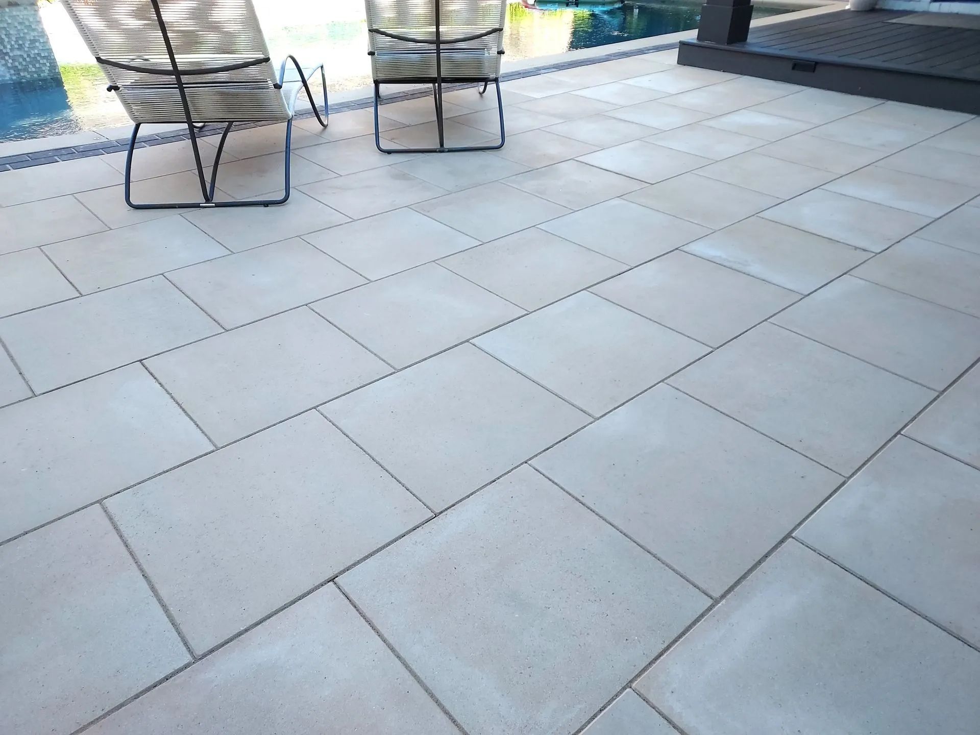 Patio with light-colored rectangular pavers, two chairs, and a glimpse of a pool.