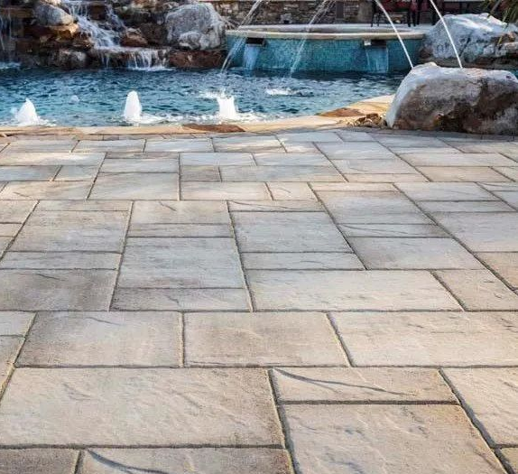 Stone patio with fountains and pool, in a residential backyard setting.