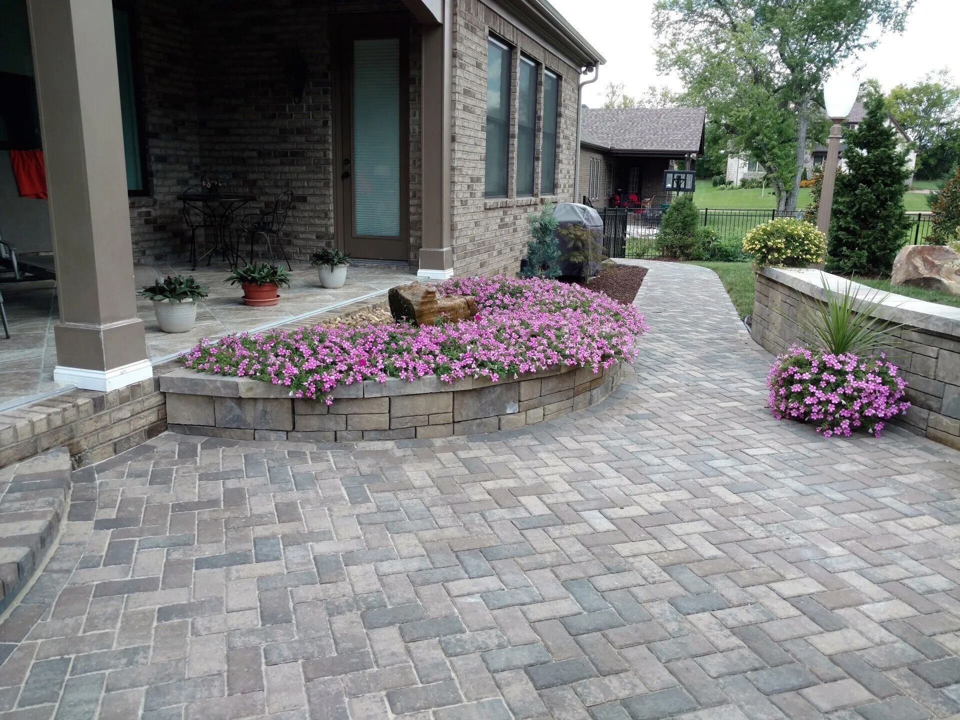 Brick patio with flower bed and walkway near a house.