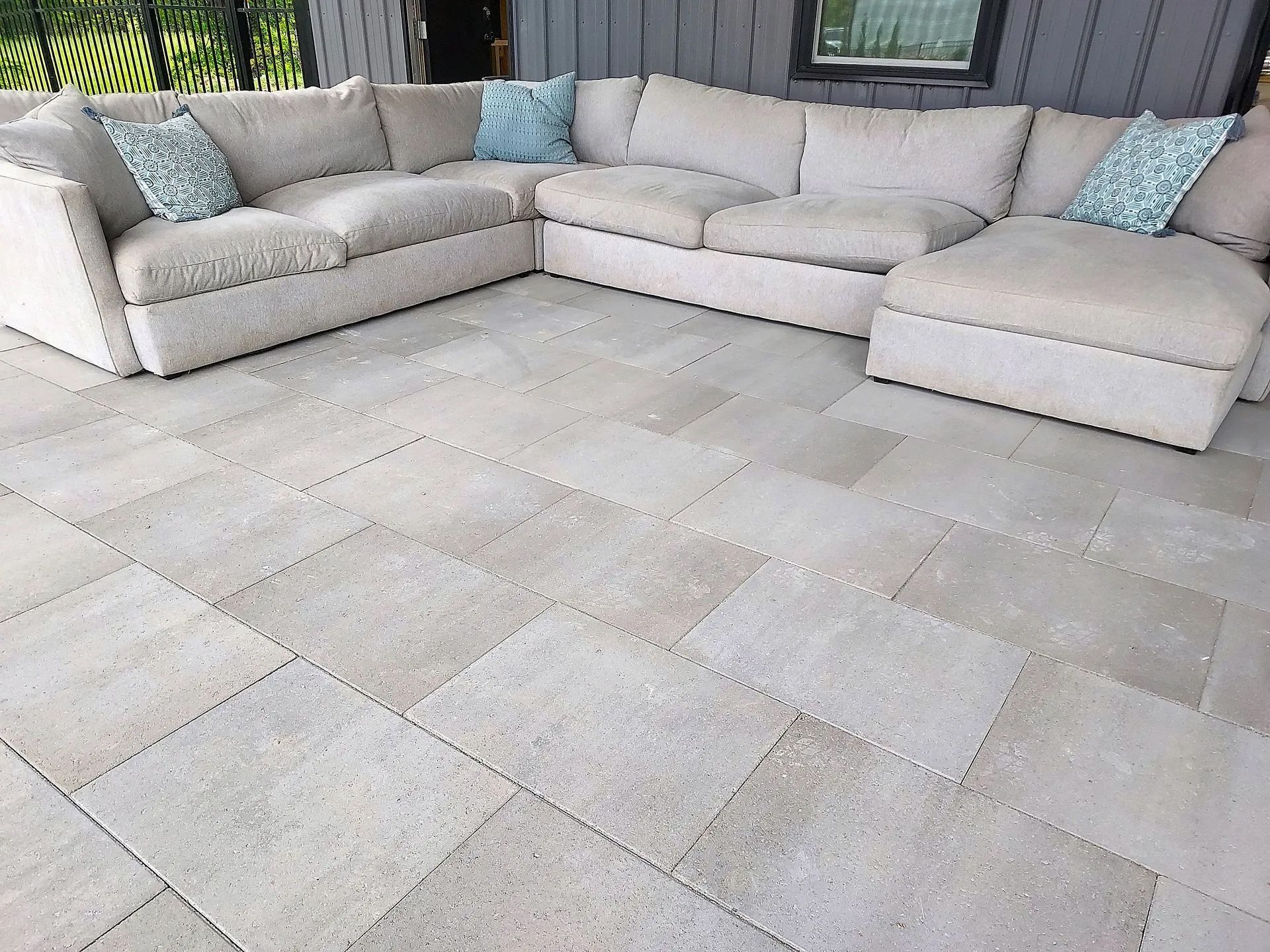 Beige sectional sofa on light stone patio with blue pillows.