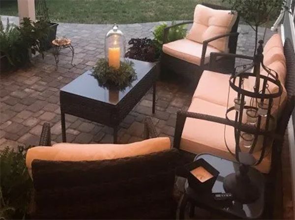 Patio furniture with tan cushions on a brick patio with a lit candle and decorative plants.