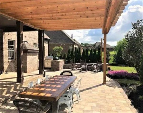 Patio with wooden pergola, dining table, and outdoor seating near a brick house. Sunny day.