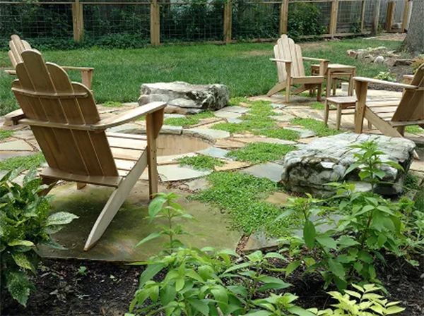 Adirondack chairs around a stone patio with fire pit, in a backyard setting.