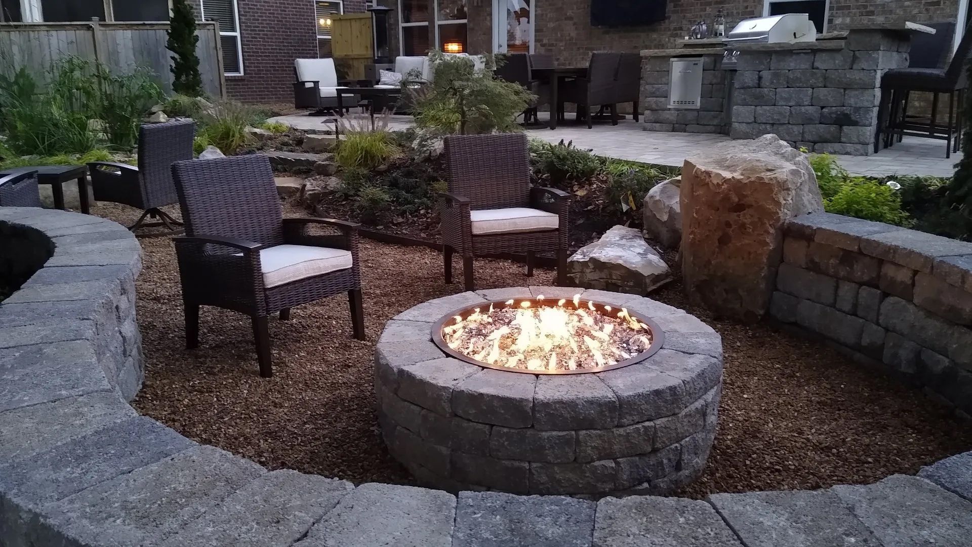 Stone fire pit with chairs in a backyard patio setting with stone retaining walls.