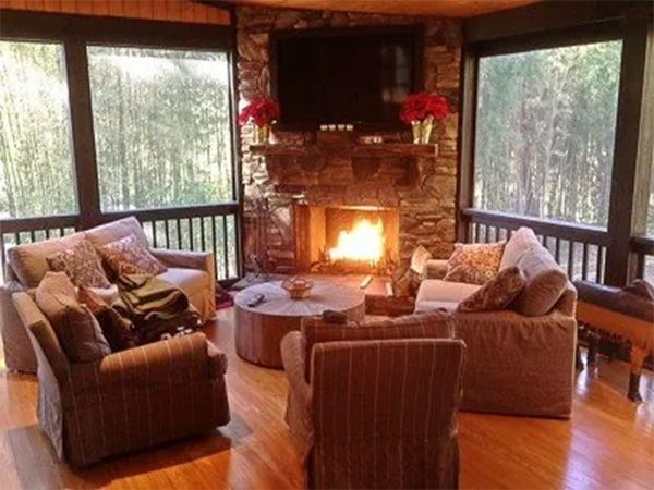 Living room with stone fireplace, TV, and four armchairs arranged around a wooden coffee table.
