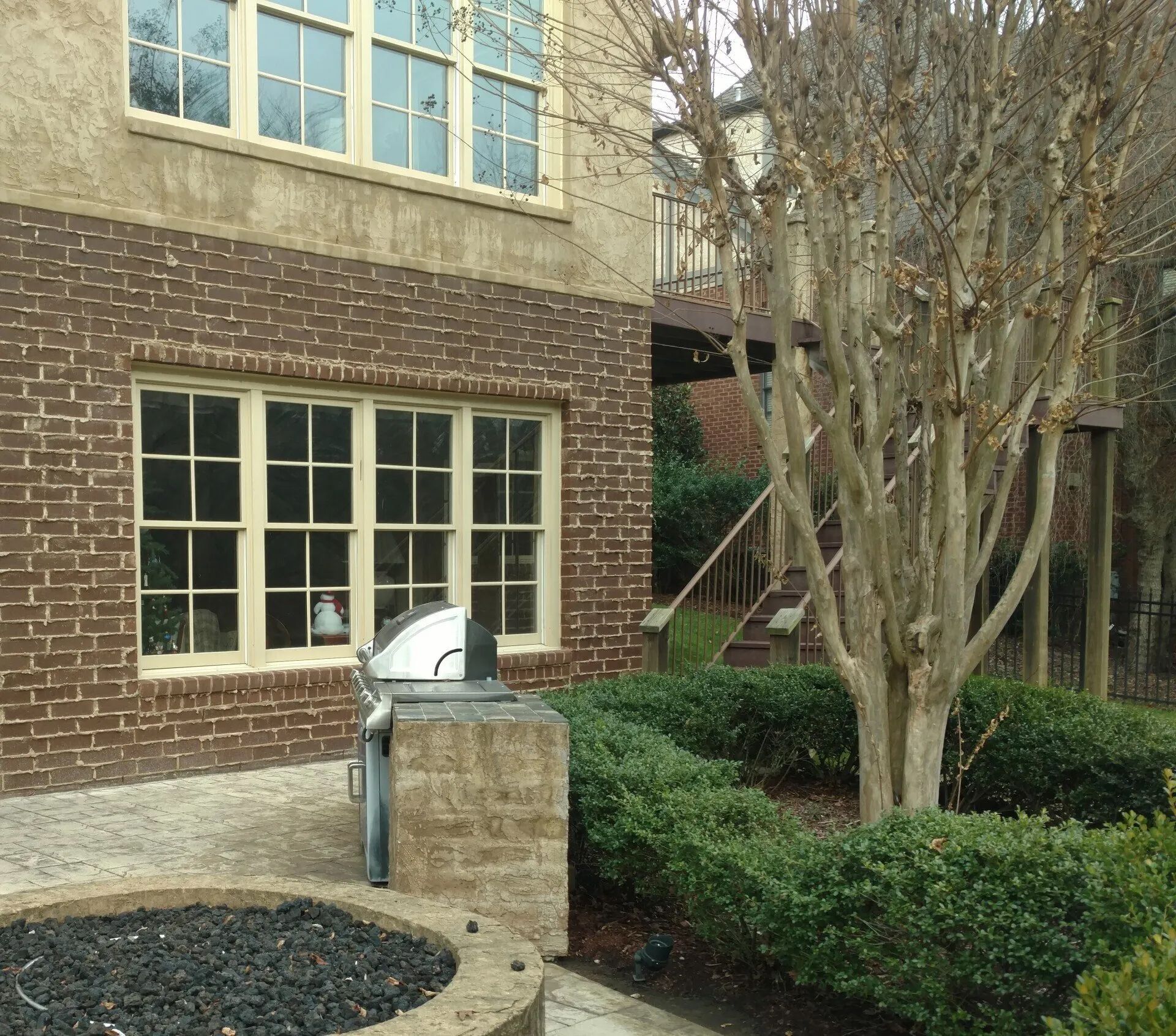Brick and stucco house exterior with windows, a grill, and landscaping.