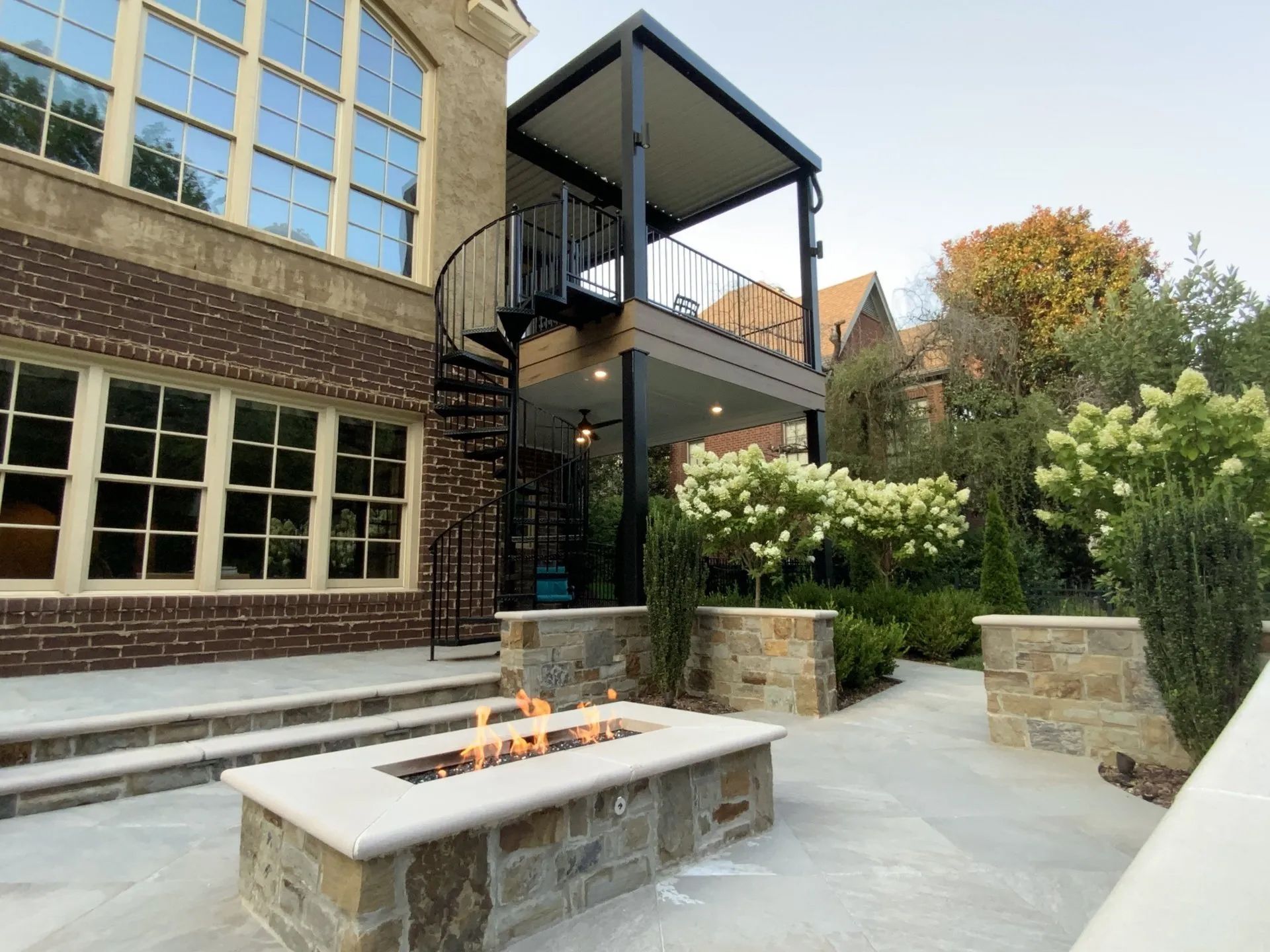 Stone patio with fire pit, deck, spiral staircase, and landscaped yard.