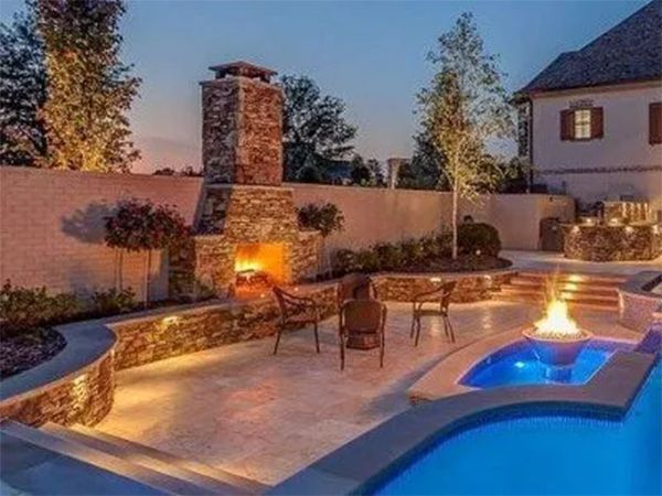 Outdoor patio with fireplace, hot tub, and pool at dusk, with ambient lighting.